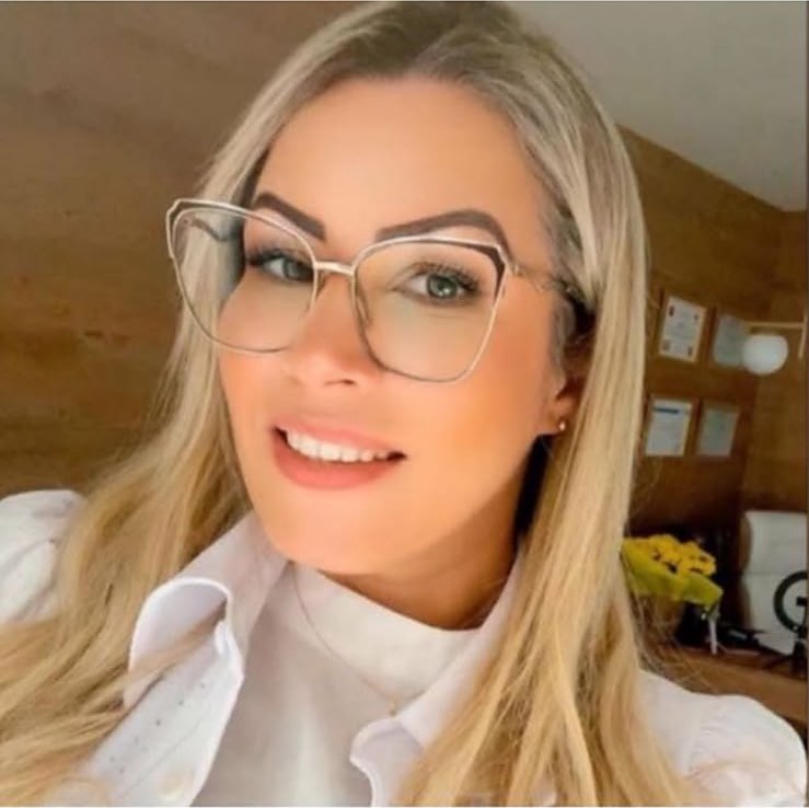 Dra. Érica Rangel sorrindo em seu consultório, de óculos e blusa branca