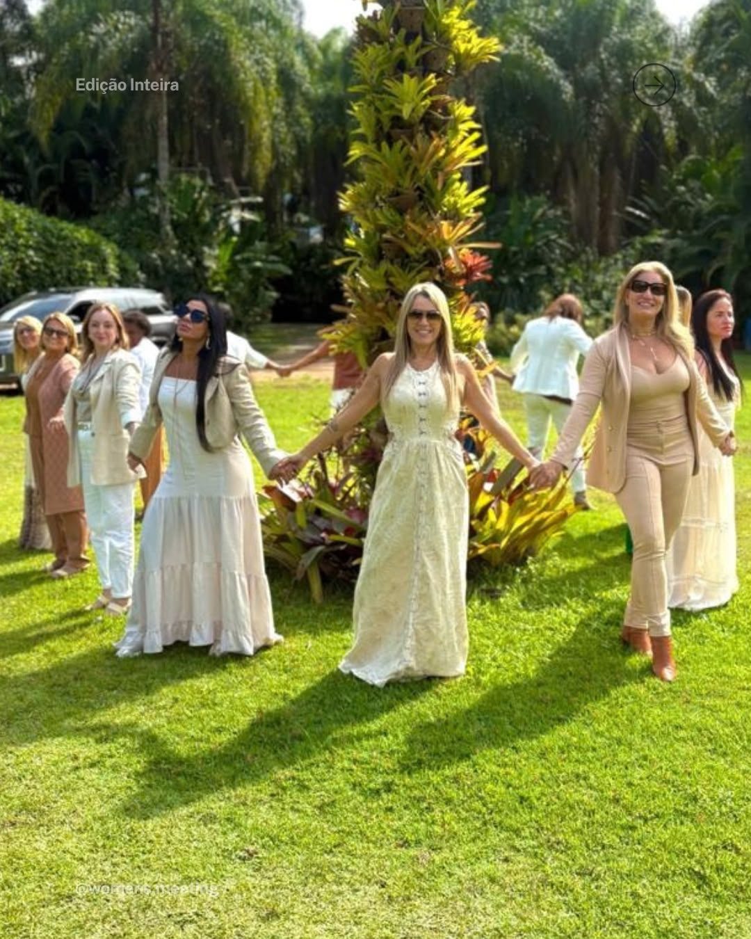 Participantes do Women’s Meeting de mãos dadas em roda ao redor de uma árvore florida